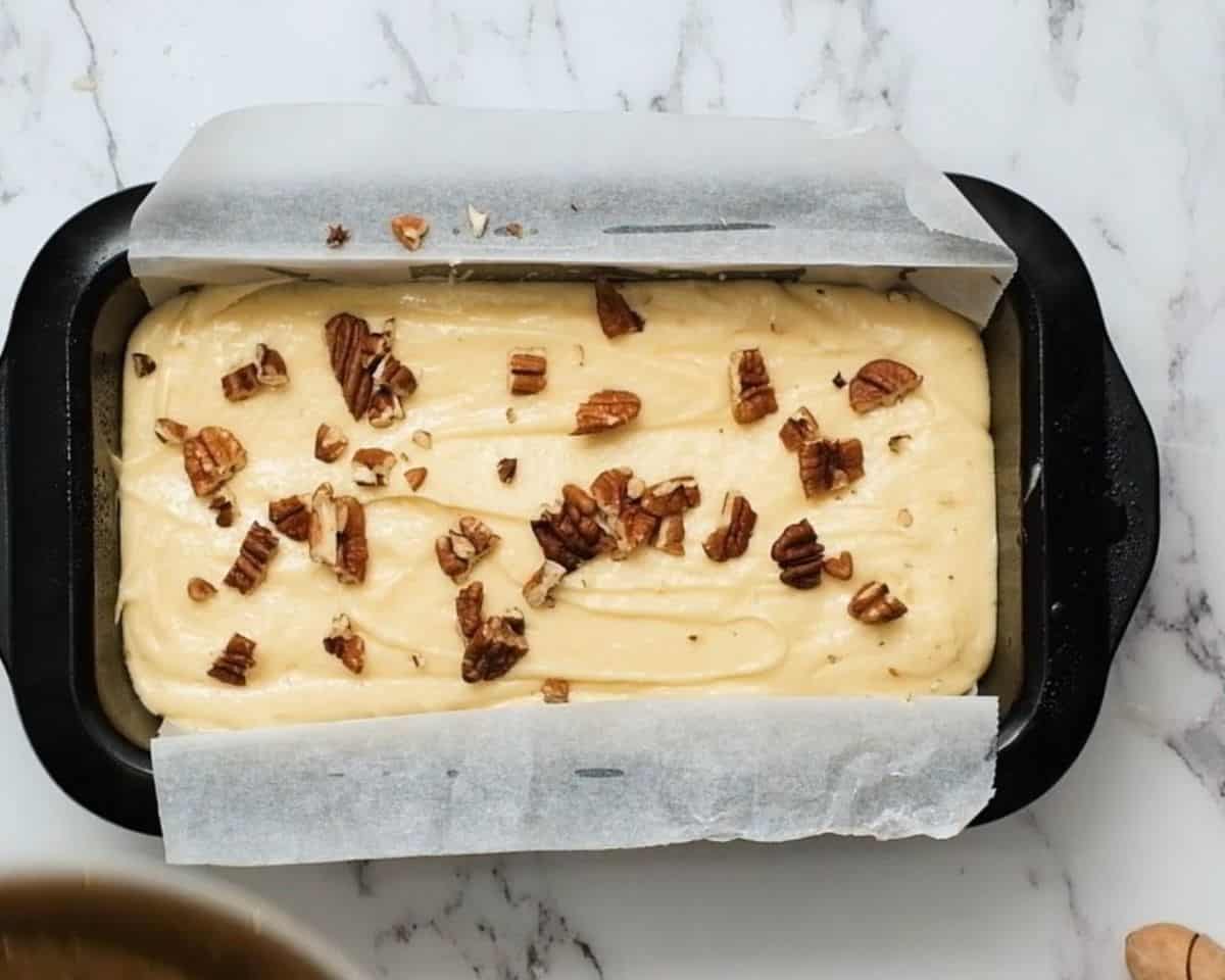 Pecan pie pound cake with pecans sprinkled on top in a loaf pan.