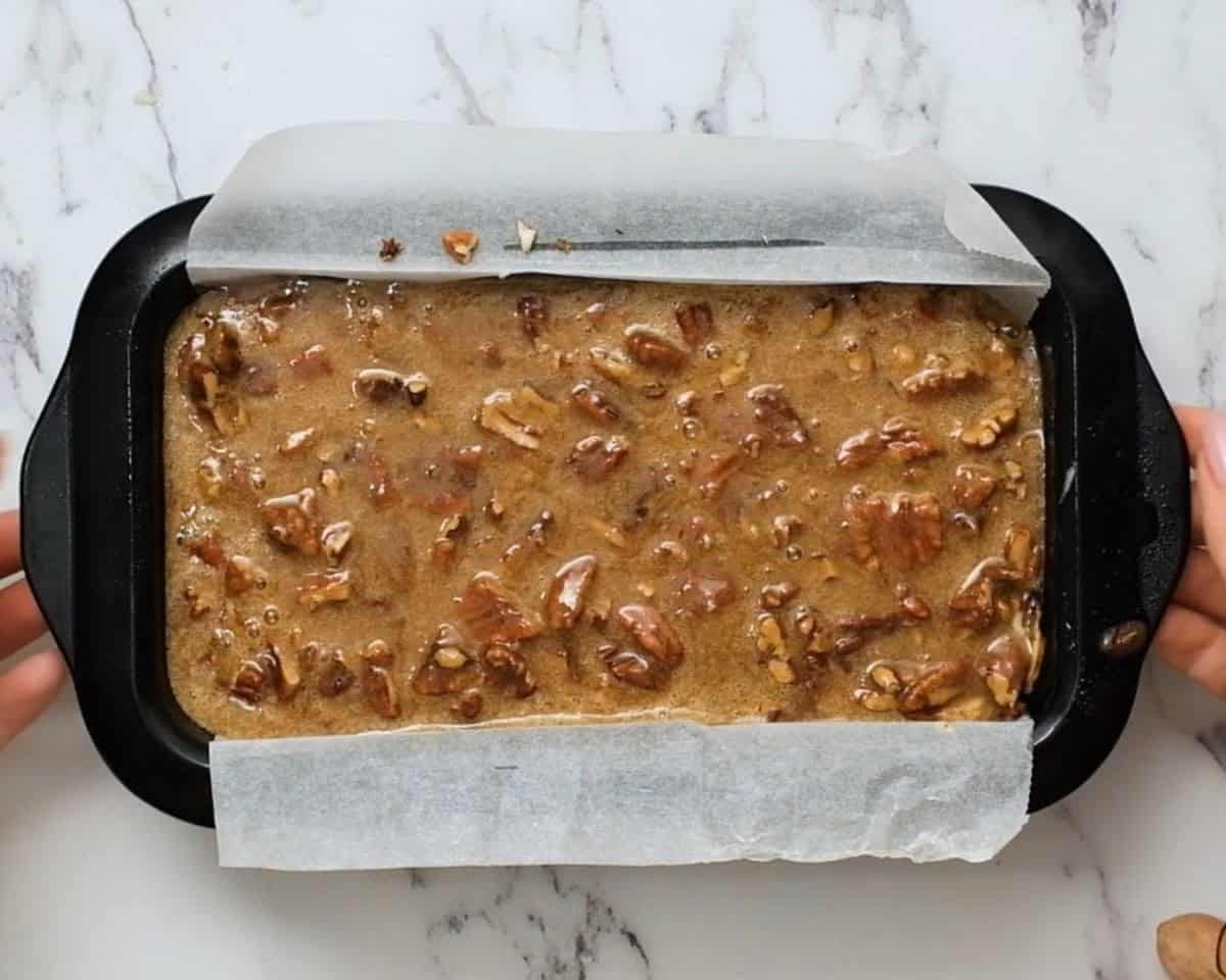 Pecan pie pound cake with pecan pie filling on top in a loaf pan.