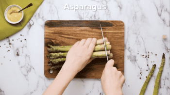 trimming asparagus with a knife on a cutting board.