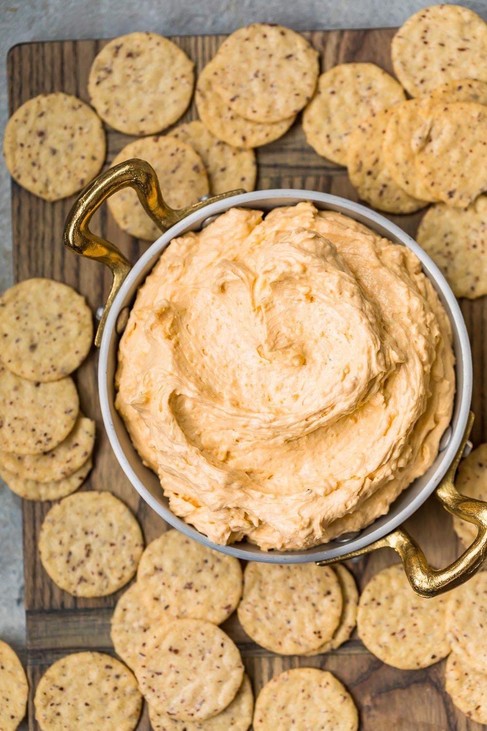 Top shot of a bowl of Beer Cheese Dip with crackers on a board