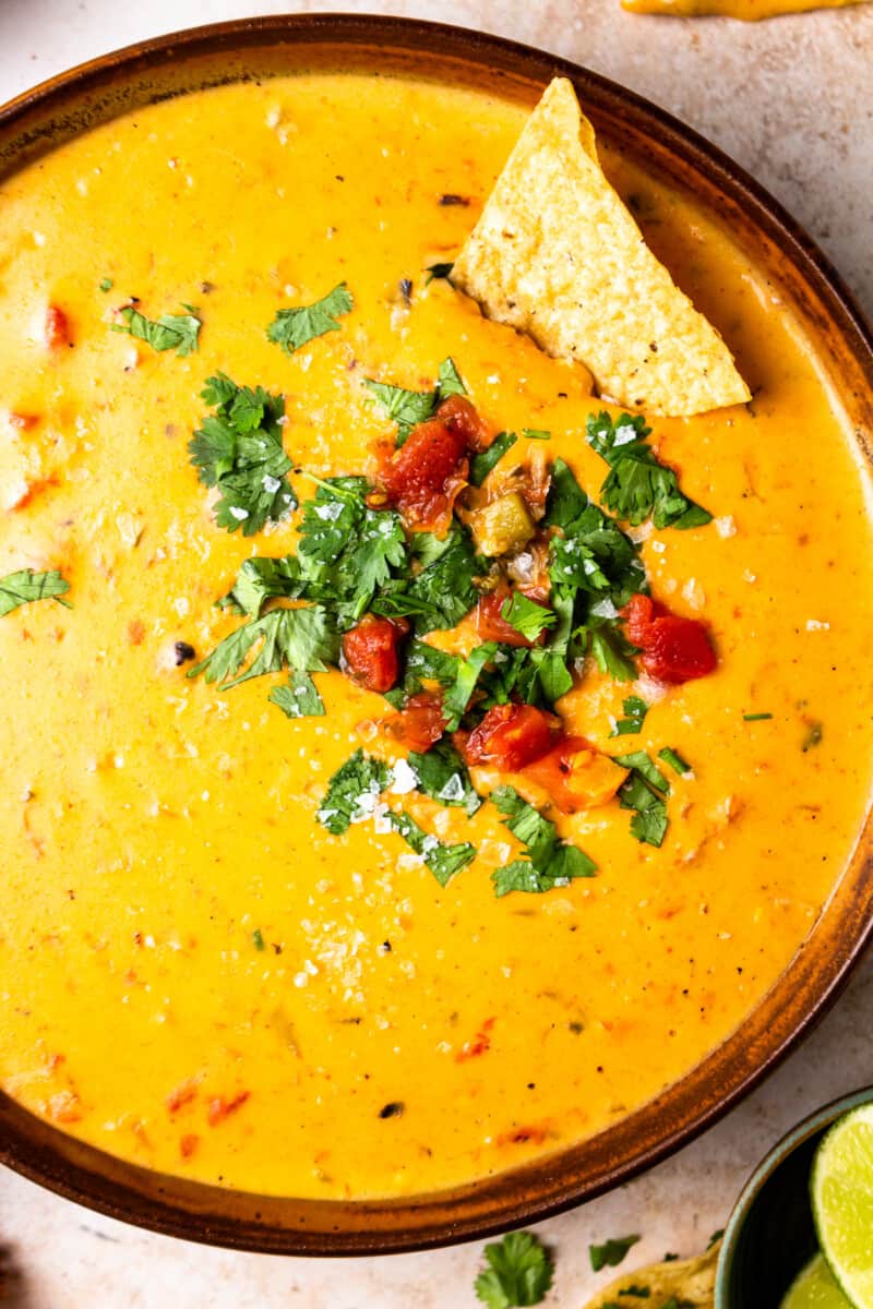bowl of crockpot queso garnished with tomatoes and cilantro with tortilla chips up close