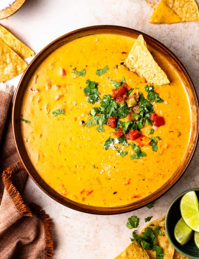 bowl of crockpot queso garnished with tomatoes and cilantro with tortilla chips