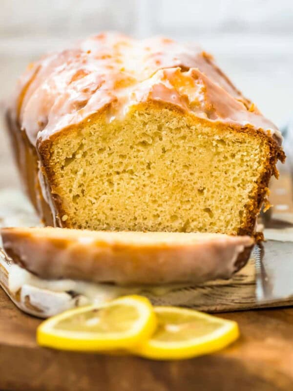 A slice of iced lemon loaf cake on a cutting board.
