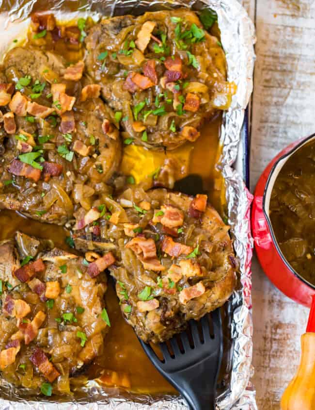 slow cooker smothered pork chops in a pan with a spatula lifting one out