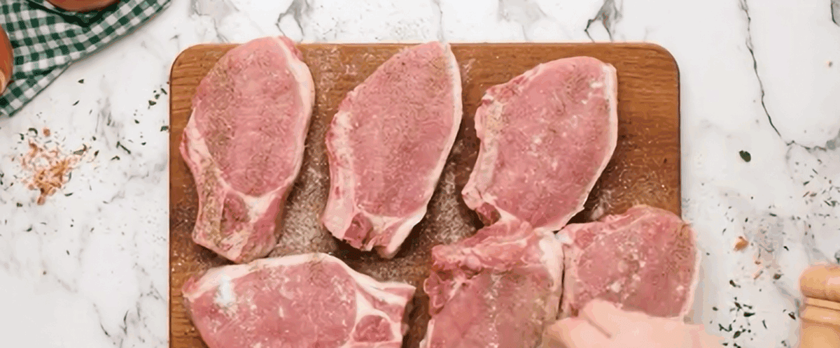 Seasoned pork chops on a wooden cutting board.