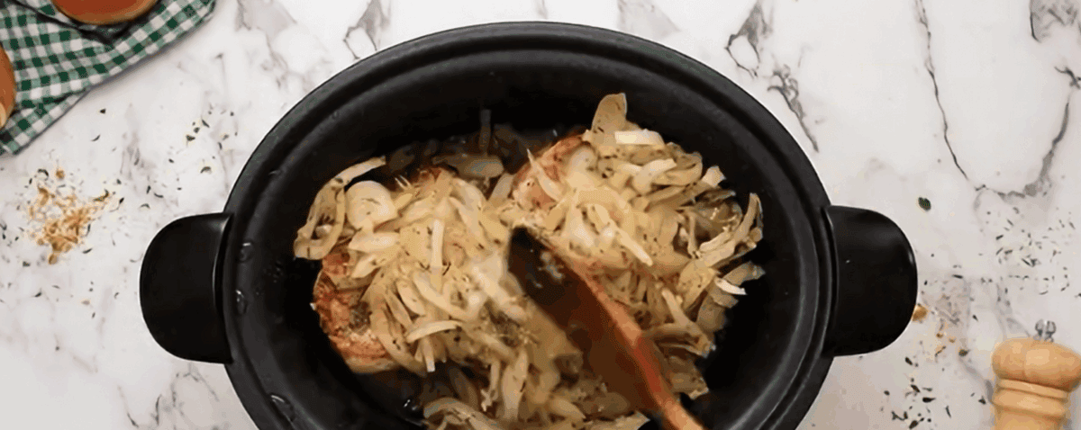 Cooked onions being placed on top of the pork chops in the slow cooker. 