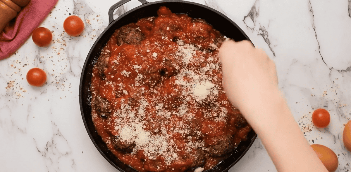 meatballs in a skillet topped with marinara sauce and Parmesan cheese. 
