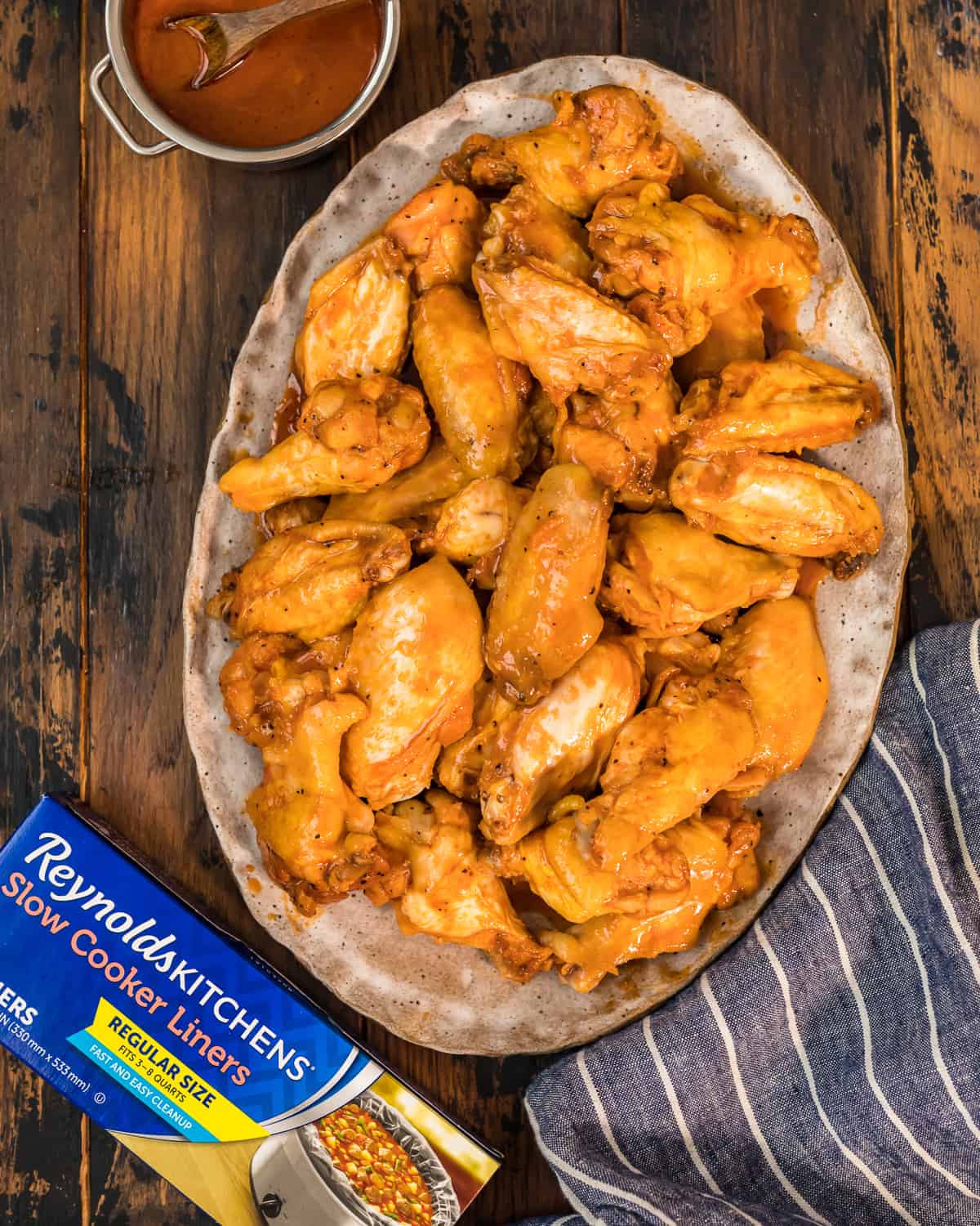 a big bowl of chicken wings next to a box reynolds slow cooker liners 