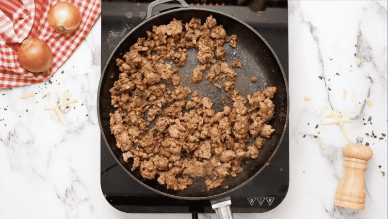 A queso fundido recipe featuring a frying pan with meat and onions sizzling on it.