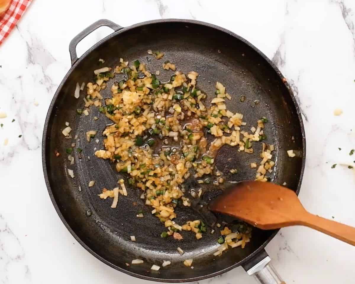 Diced onion, jalapeño, and garlic sautéing in a cast iron skillet for queso fundido.