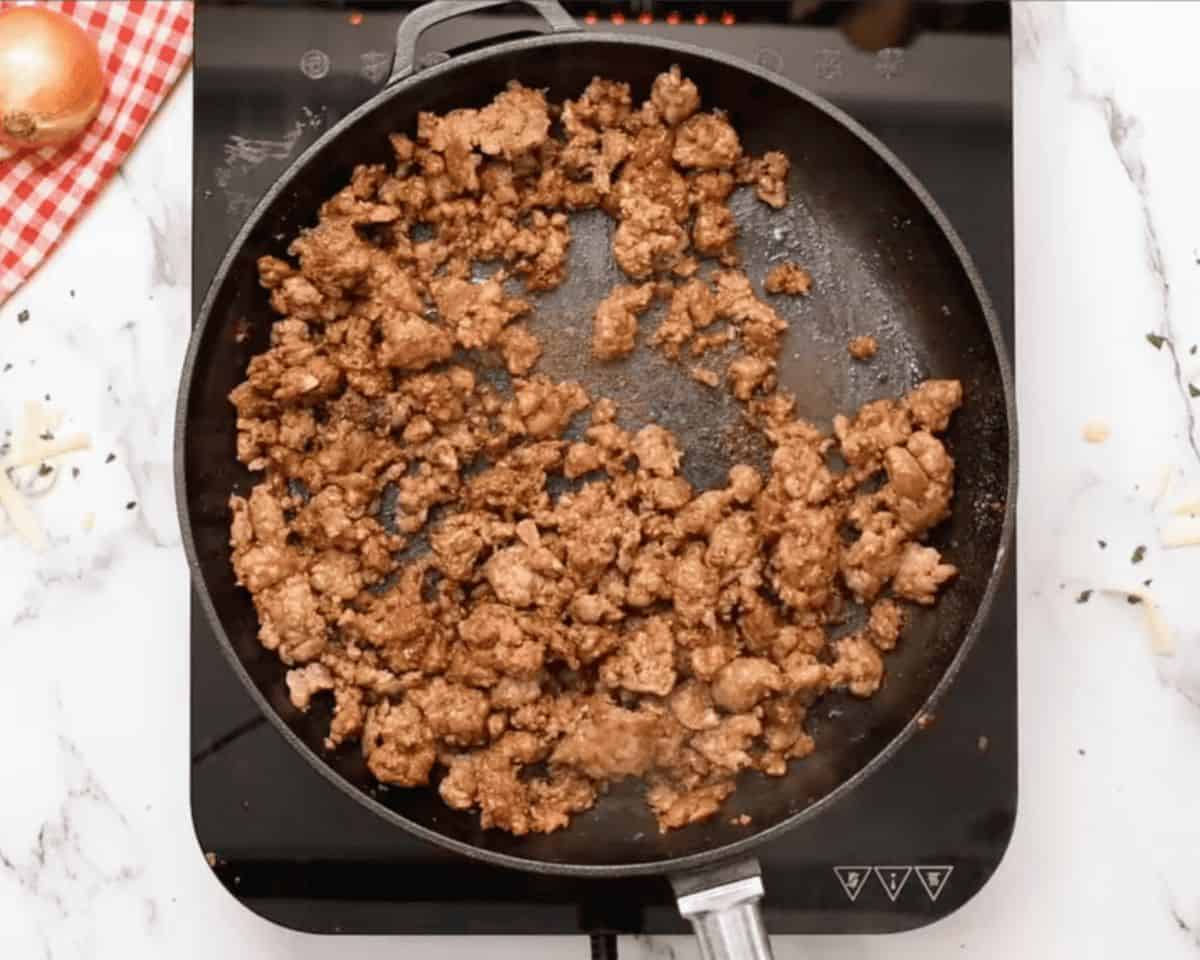 Browned chorizo sausage cooking in a cast iron skillet for queso fundido.