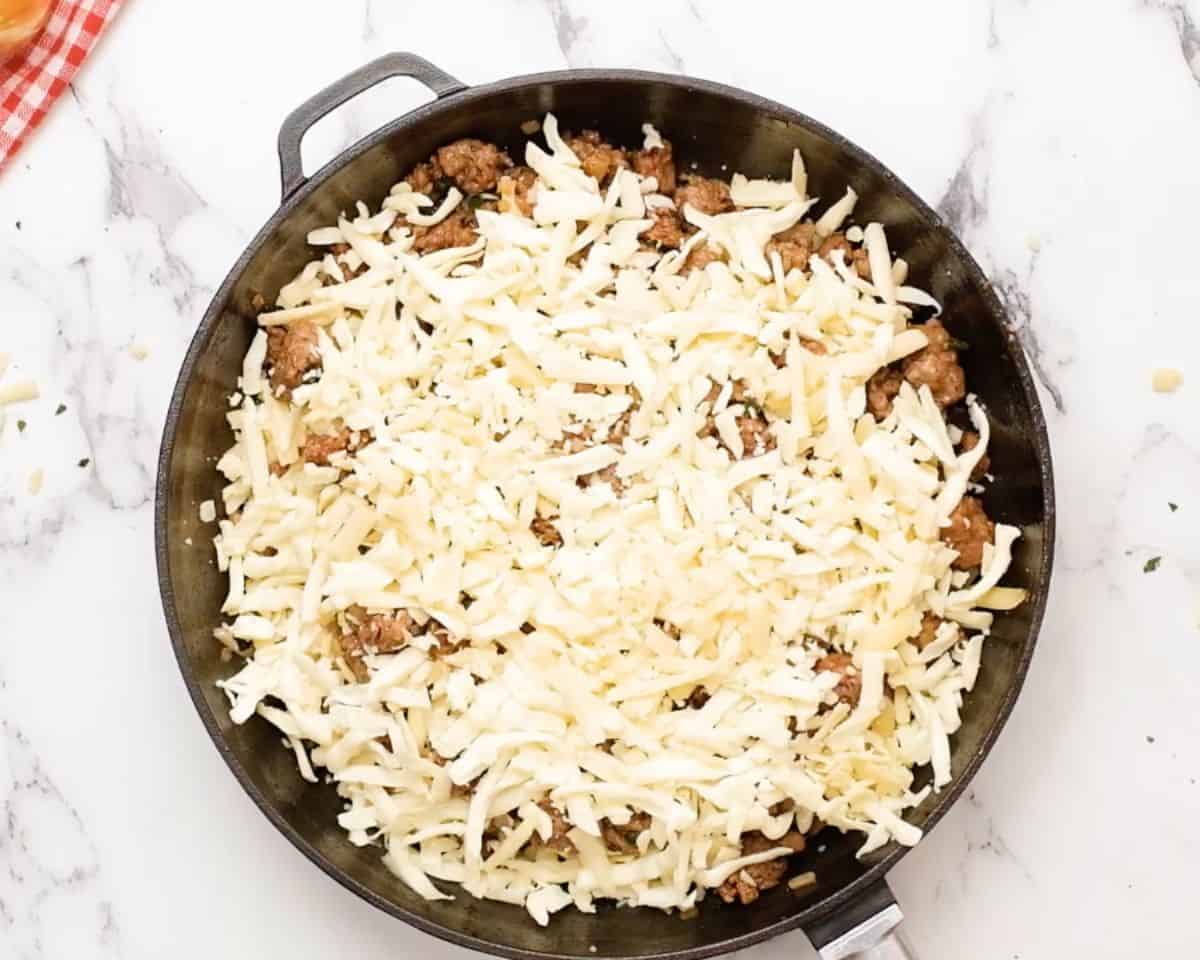 Layered queso fundido with shredded cheese covering the chorizo mixture before baking.