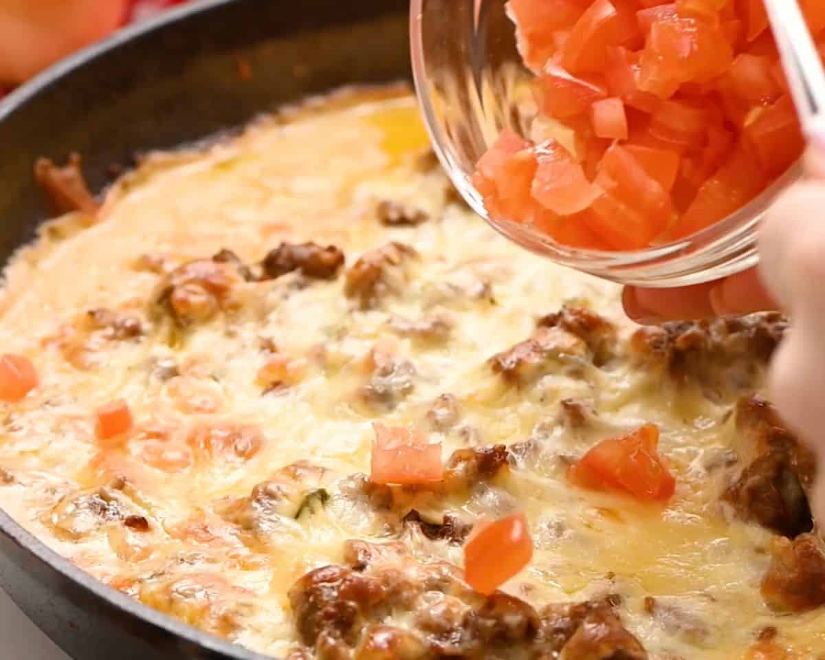 Spoonful of diced Roma tomatoes being added over hot, bubbly baked queso fundido.