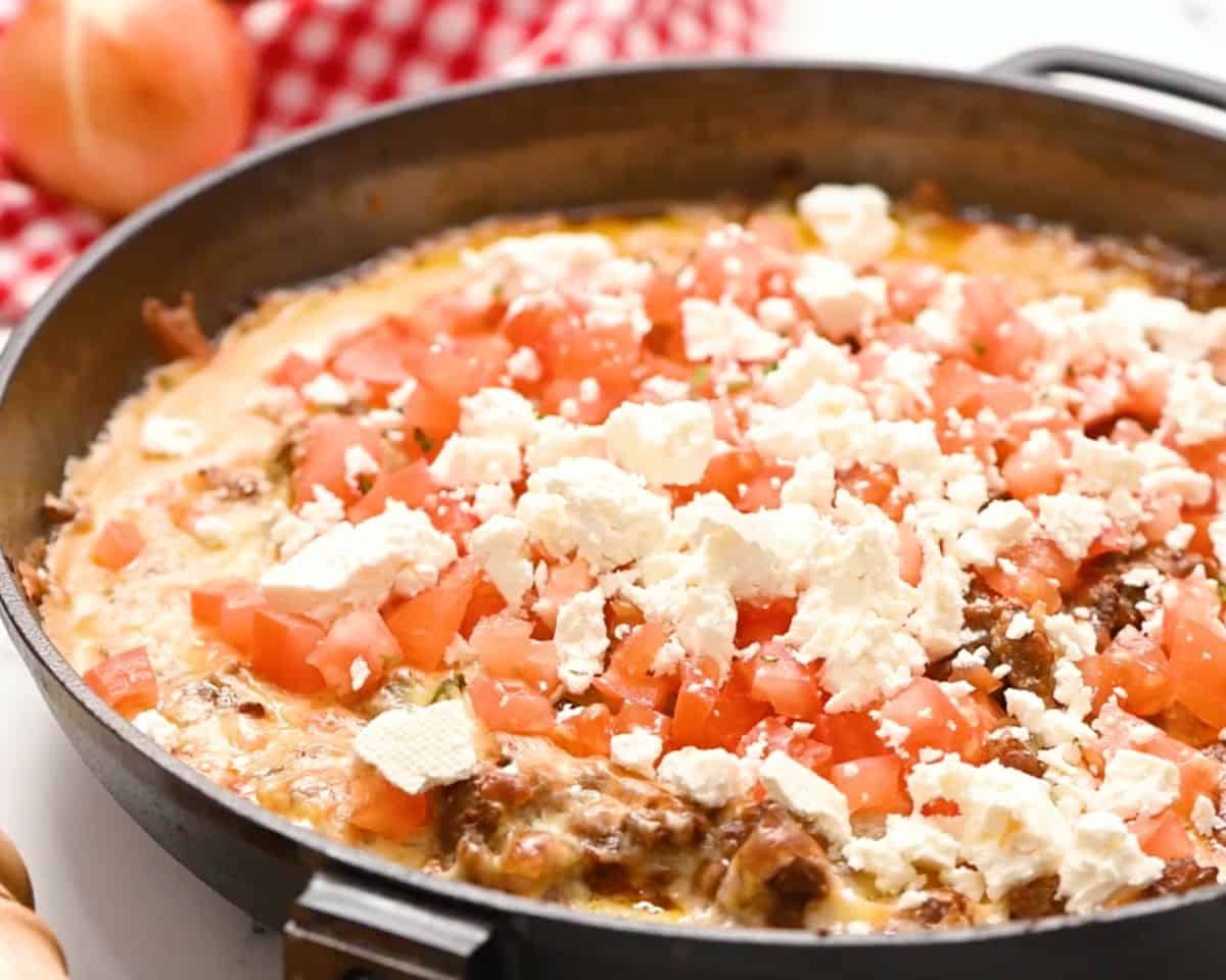 Baked queso fundido topped with diced tomatoes and crumbled queso fresco in a cast iron skillet.