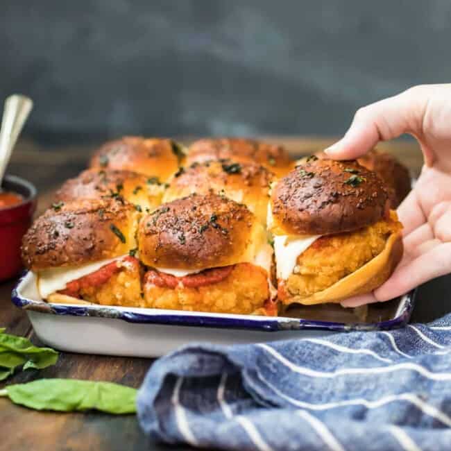 A person holding a Chicken Parmesan Slider on a baking sheet.
