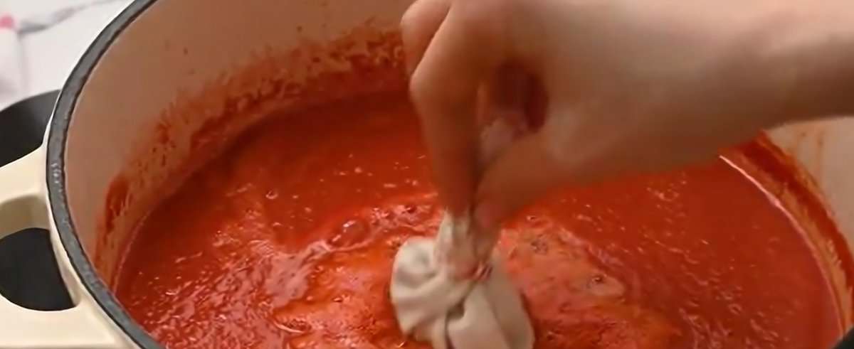 Adding an herb bag to the tomato soup in the pot.