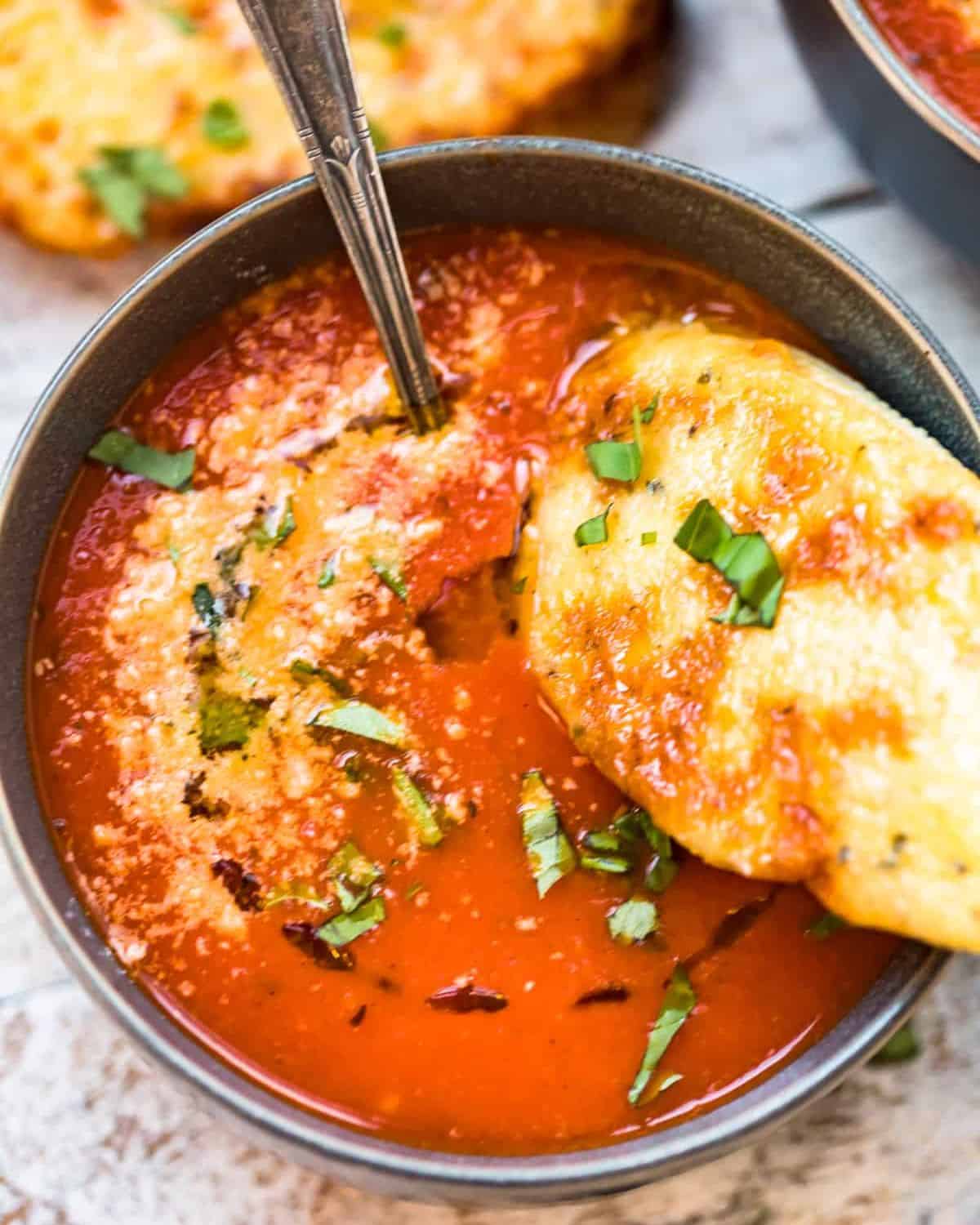 Tomato soup in a bowl with a spoon and cheese crostini.