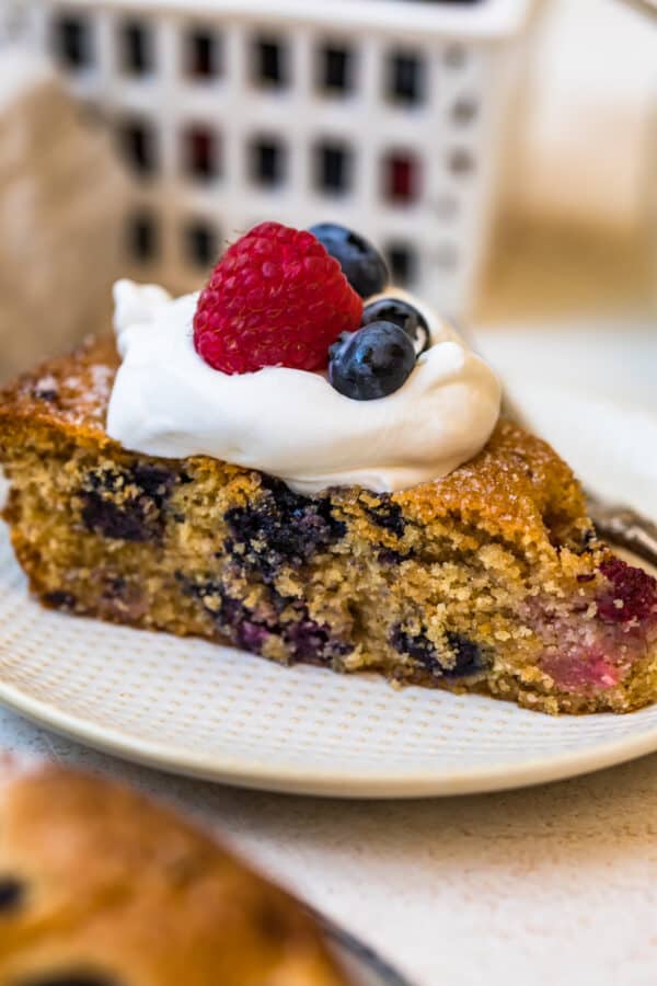 Blueberry Raspberry Coffee Cake served on a white plate with cream and fresh fruits