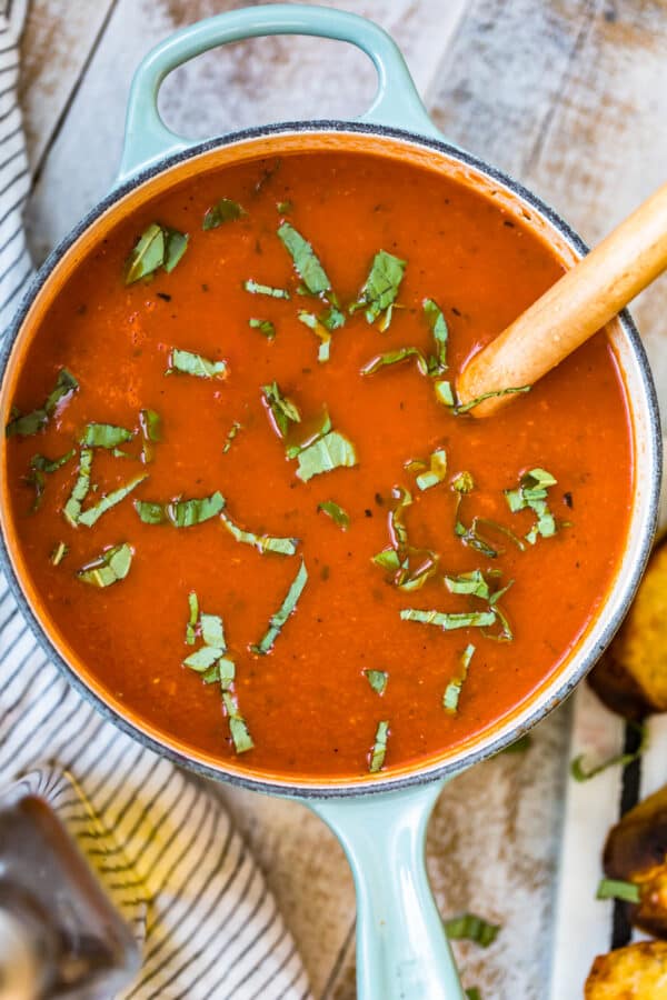 overhead view of tomato soup cooking in a pot with bits of basil on the surface