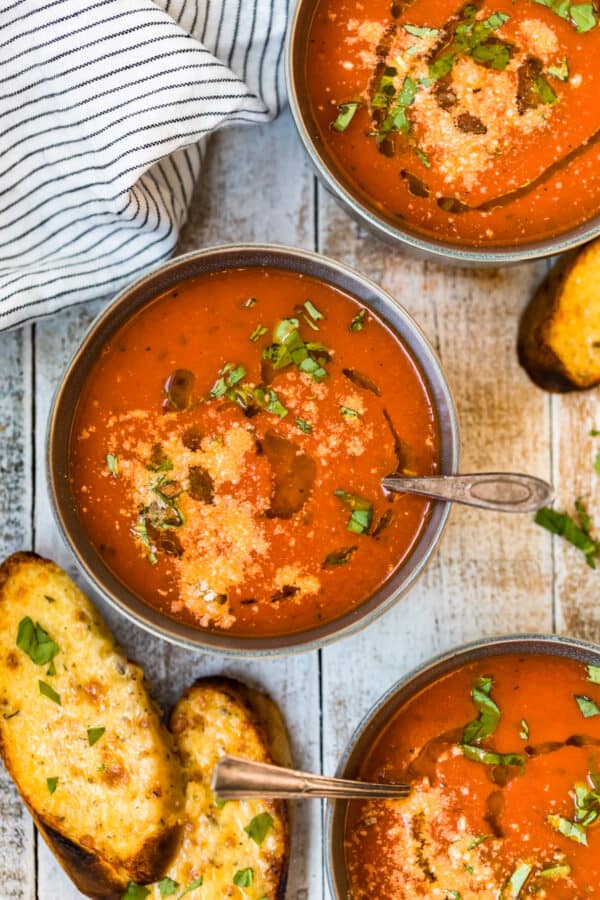 bowls of creamy tomato soup with pieces of cheesy bread on a tablescape