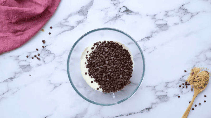 A glass bowl filled with chocolate chips and a wooden spoon, perfect for making a delicious chocolate bundt cake.