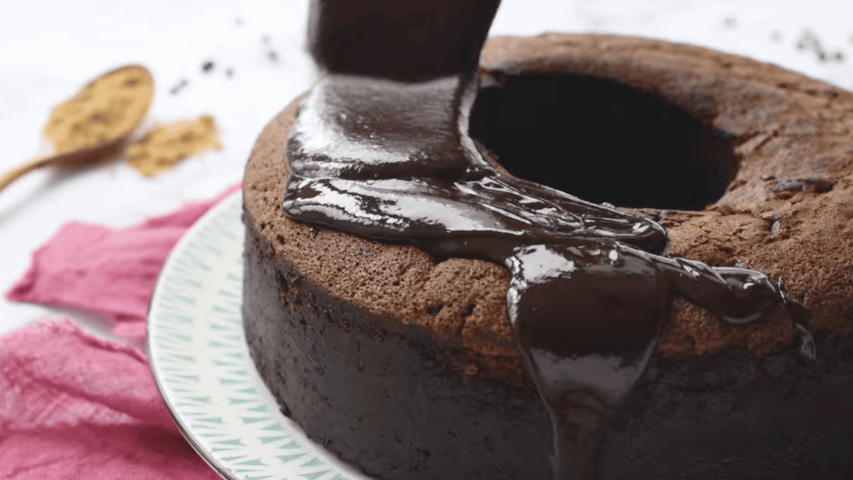 chocolate ganache poured over chocolate bundt cake on a white plate.