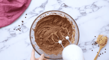 a person mixing chocolate cake batter in a glass bowl with a hand mixer.