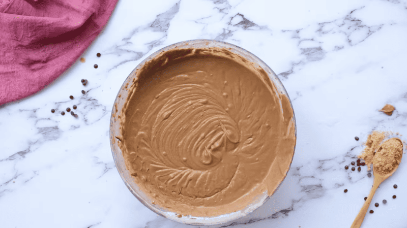 A bowl of peanut butter next to a chocolate bundt cake on a marble countertop.