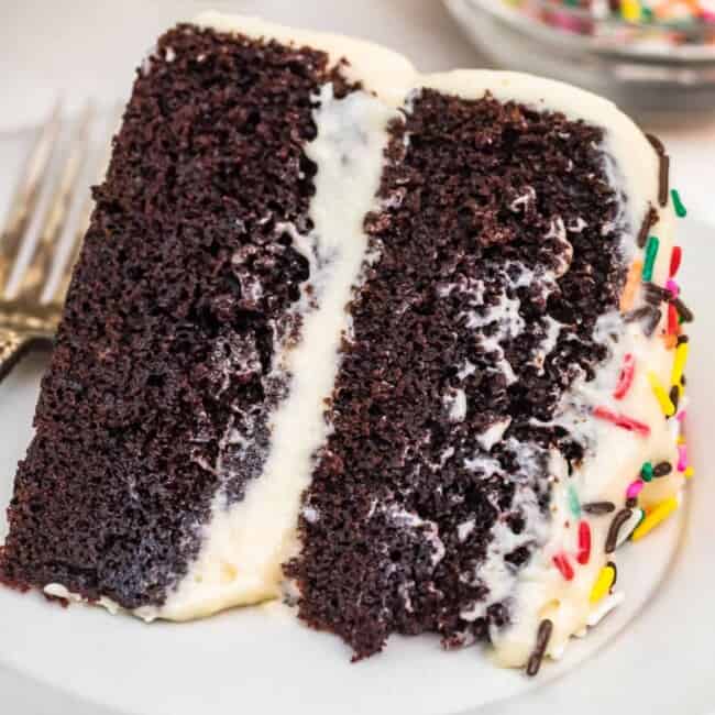 A piece of chocolate cake on a plate, with Icing and Cookie