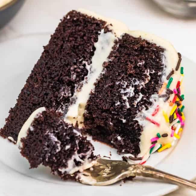 A piece of chocolate cake on a plate, with Icing and fork