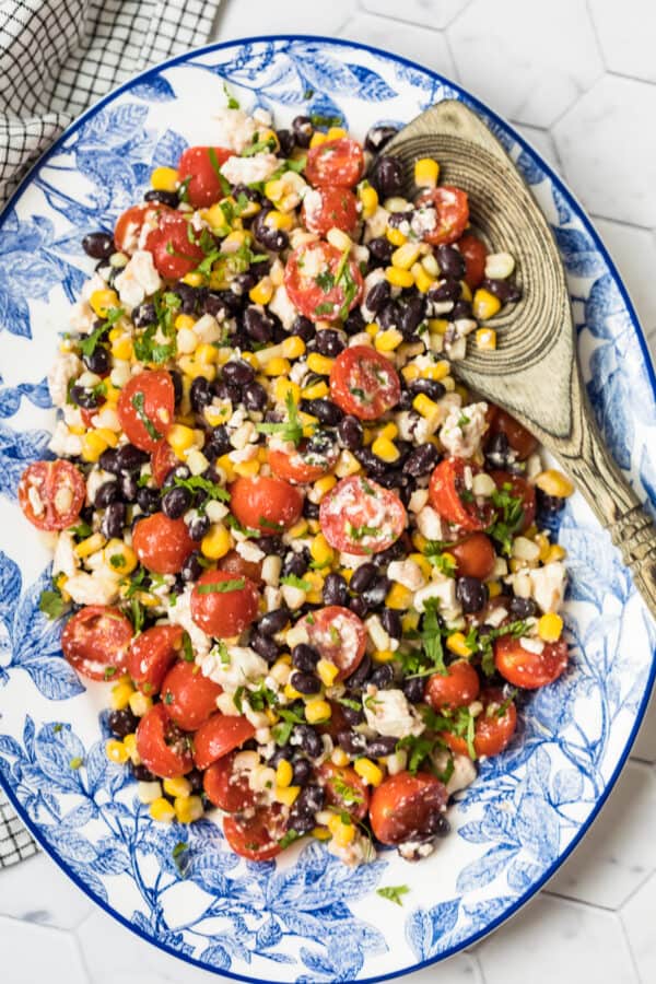 tomato corn salad on platter with wooden spoon