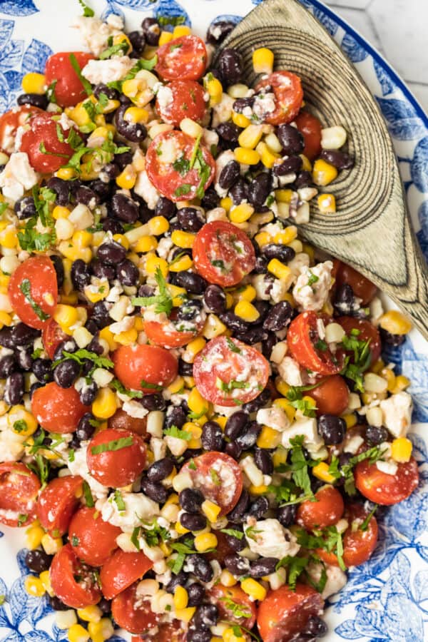 tomato corn salad on platter with wooden spoon