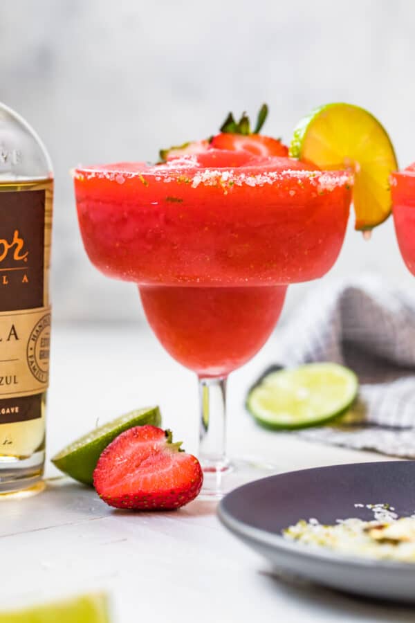 frozen strawberry margarita in glass next to tequila