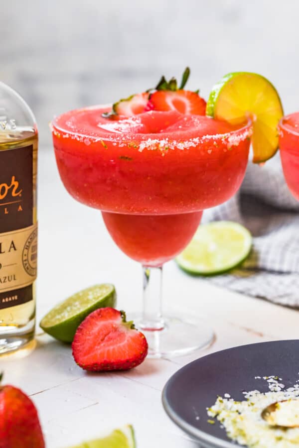 frozen strawberry margarita in glass next to tequila