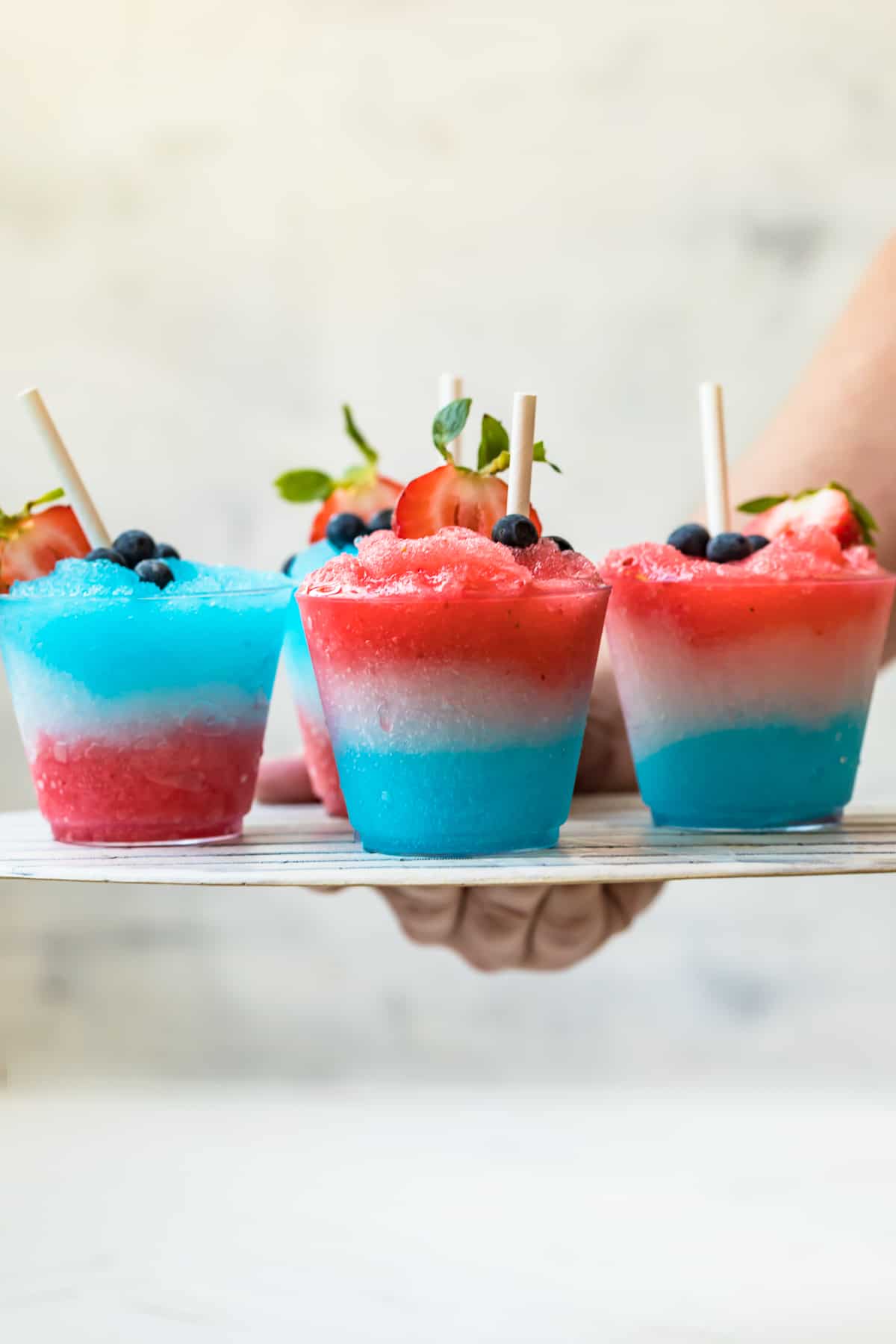 hand holding up platter of red white and blue margarita slushies for 4th of july