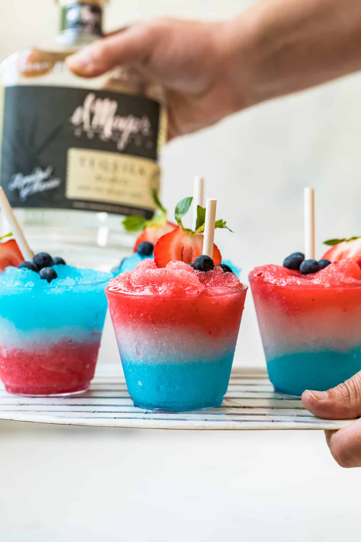 hand holding up platter of red white and blue margarita slushies for 4th of july