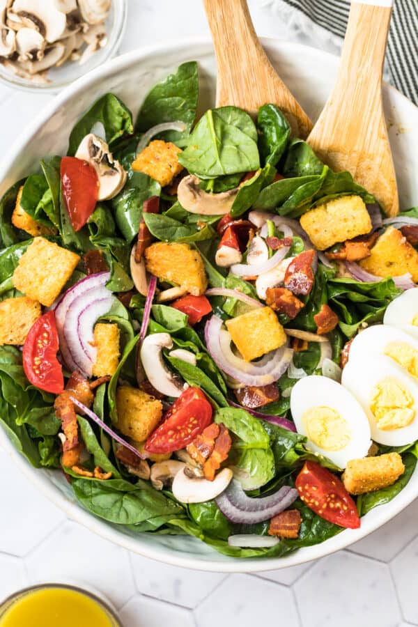 spinach bacon salad with spinach salad dressing in white bowl