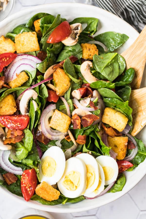 up close image of spinach salad in bowl with wooden spoons