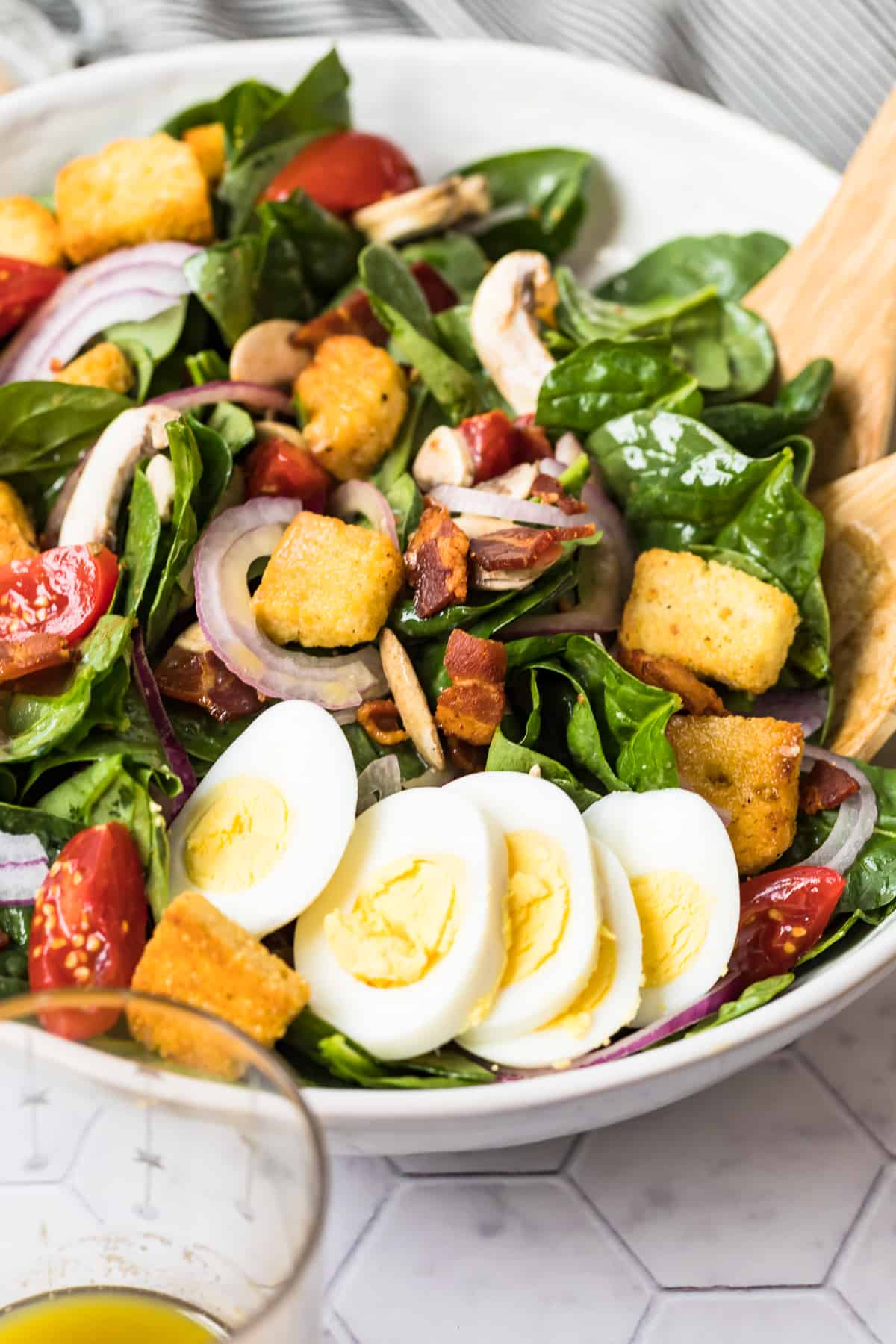up close image of spinach salad in bowl with wooden spoons