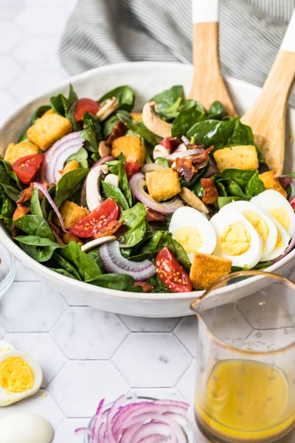 side shot of spinach salad with bacon and hard boiled egg in white bowl