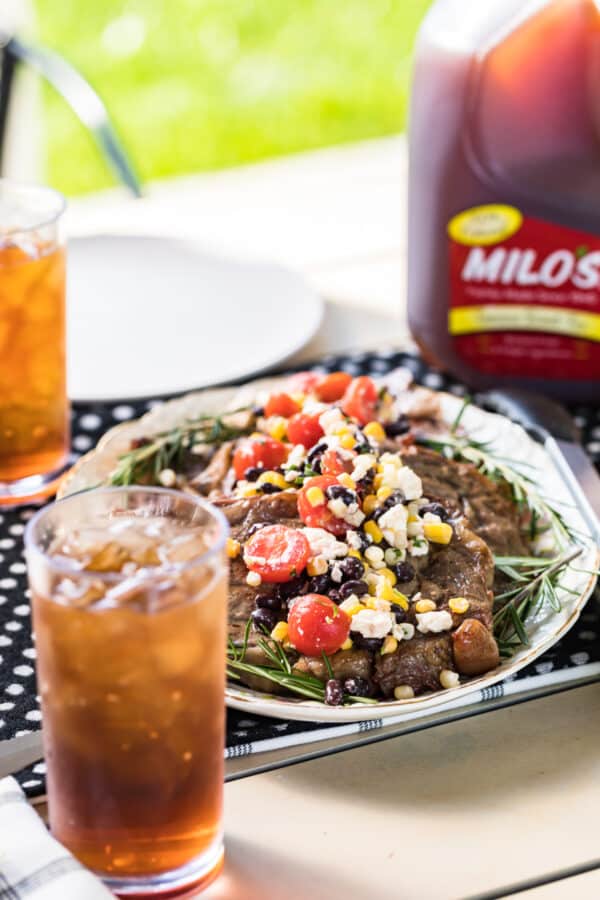 grilled ribeyes topped with corn salad on platter