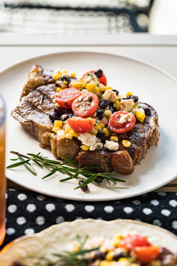 grilled ribeye topped with tomatoes and corn on plate