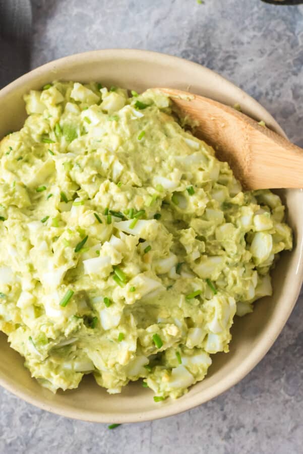 avocado egg salad in bowl with wooden spoon