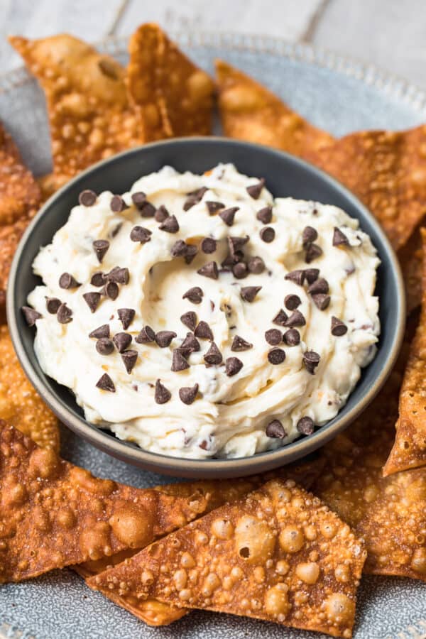 cannoli dip in black bowl surrounded by wonton chips