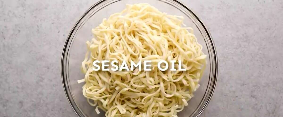 Noodles tossed in sesame oil in a glass bowl.