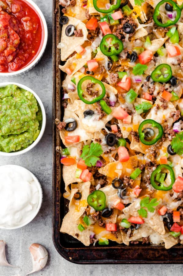baked beef nachos next to sour cream, salsa, and guacamole