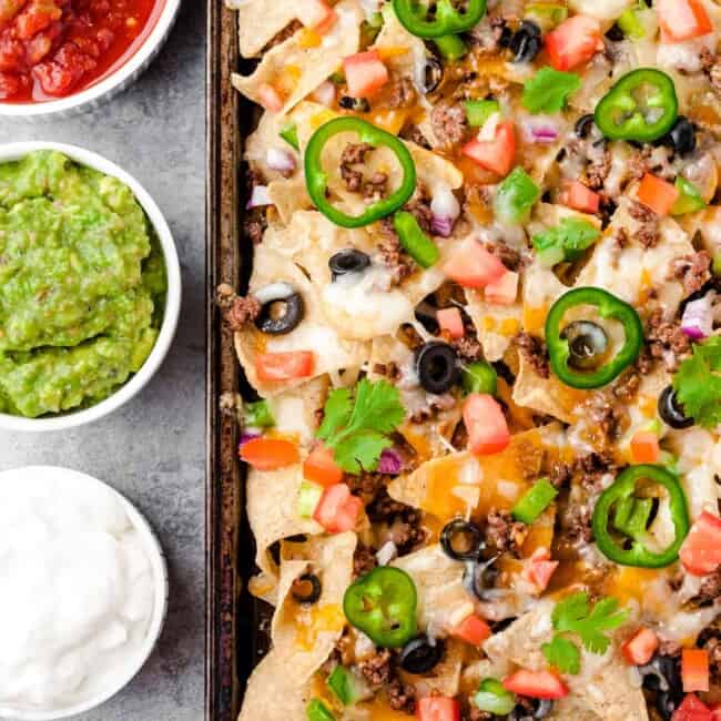 baked beef nachos next to sour cream, salsa, and guacamole