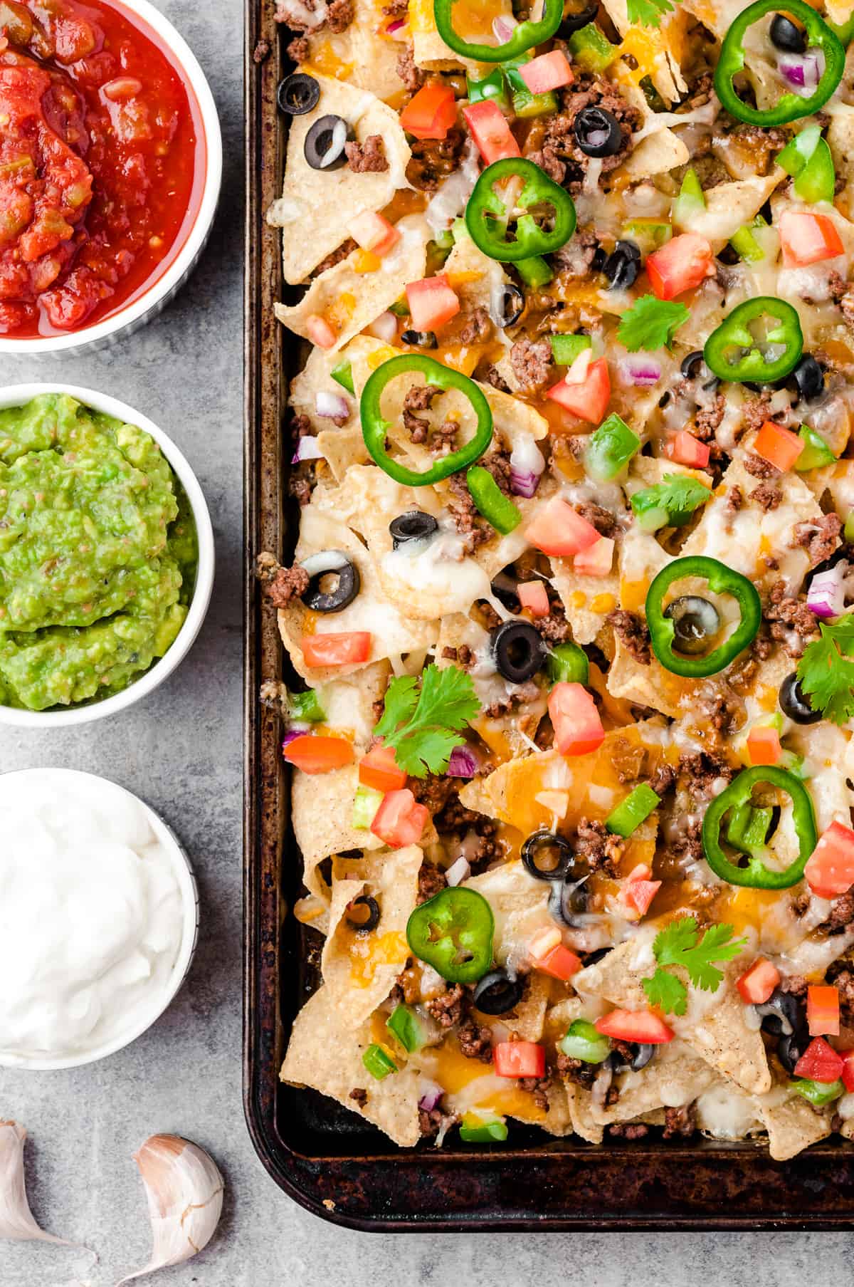 baked beef nachos next to sour cream, salsa, and guacamole