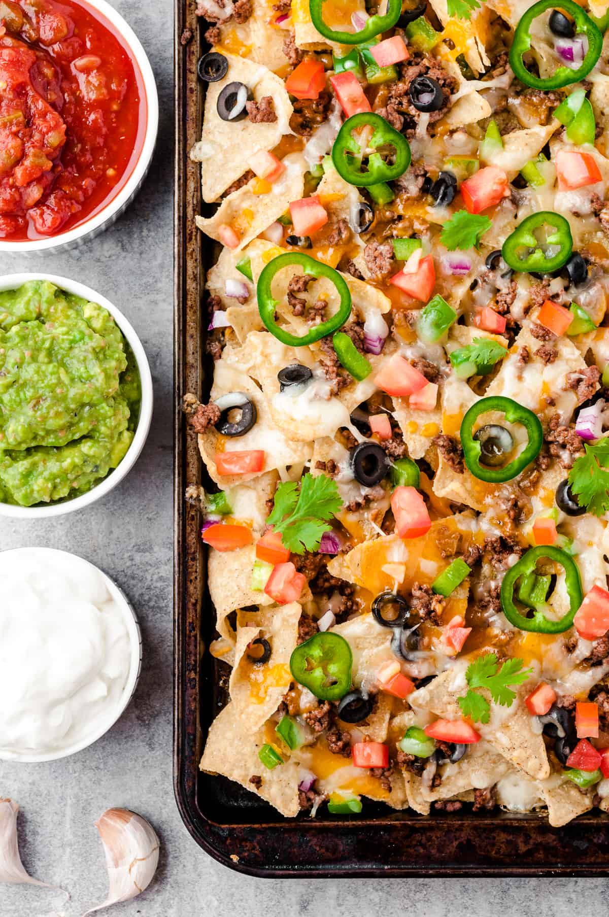 baked beef nachos next to sour cream, salsa, and guacamole
