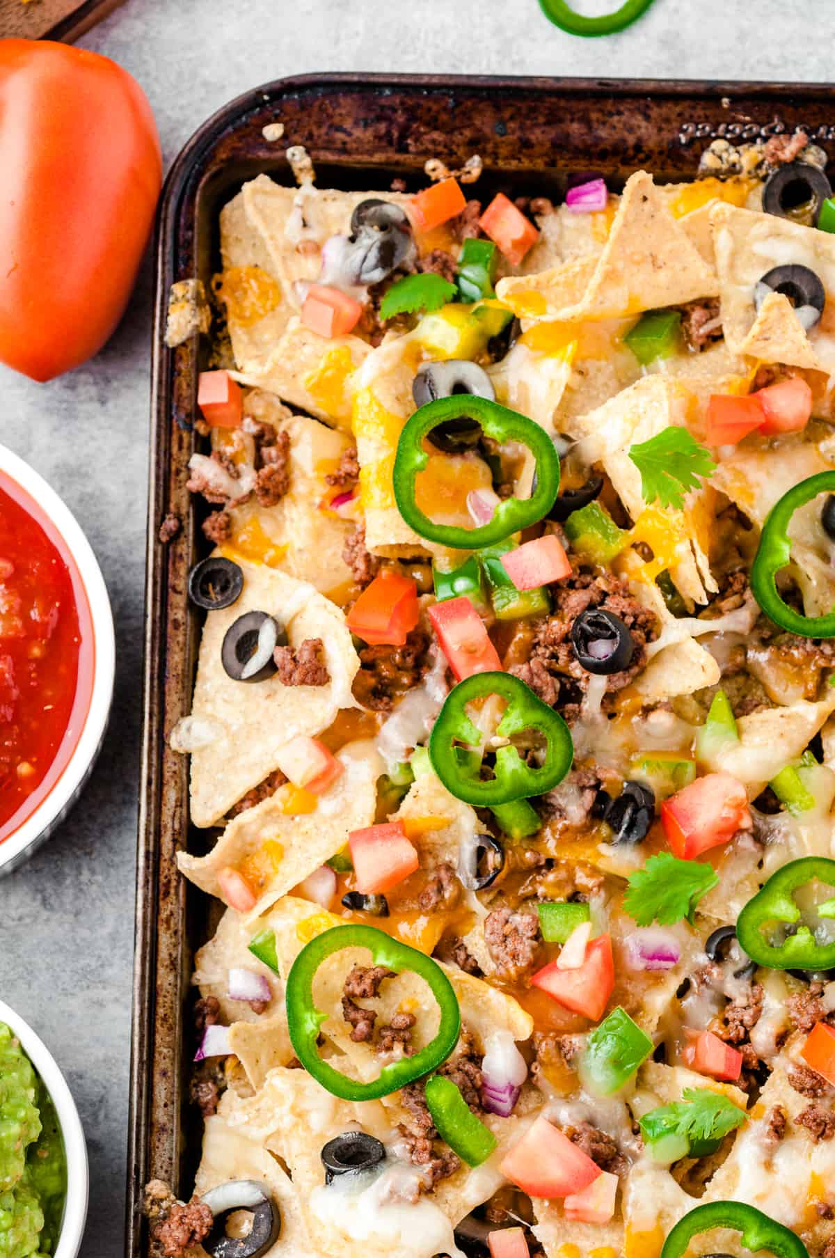 baked beef nachos next to sour cream, salsa, and guacamole